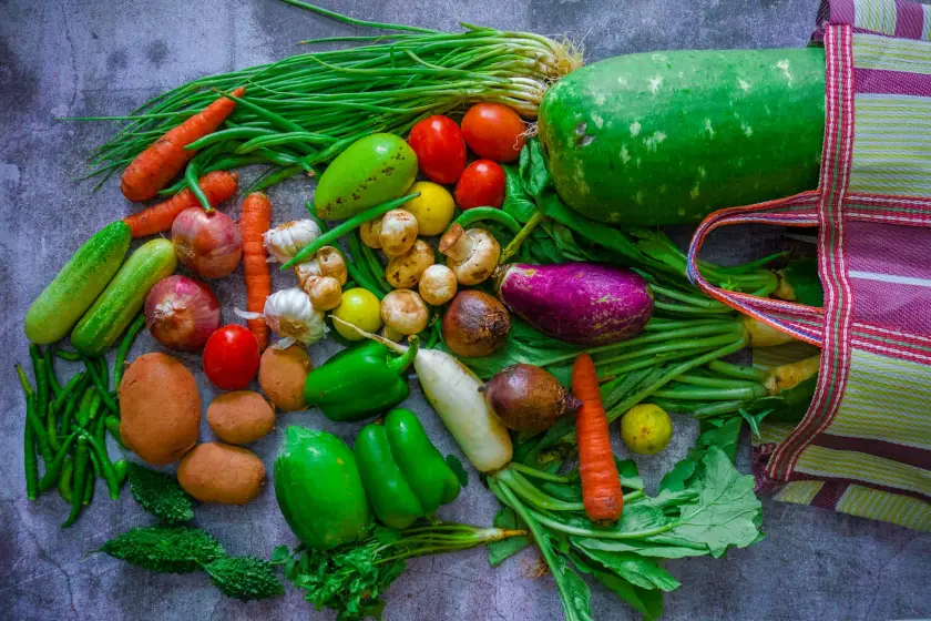 Fresh vegetables on a grey surface beside a shopping bag